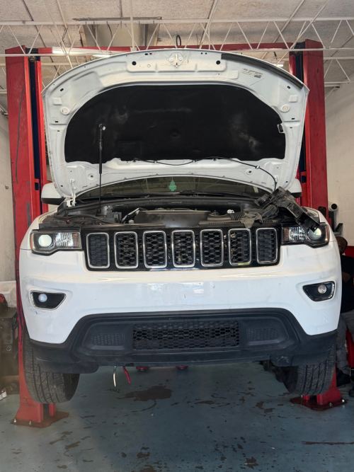 White Jeep Grand Cherokee raised on a red lift with the hood open during A/C service